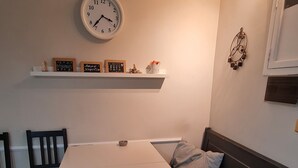 Un coin repas avec une table blanche, des chaises, un banc, une horloge et des objets décoratifs placés sur une étagère.