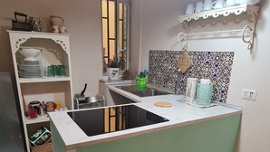 Une cuisine dotée d’un îlot central, d’un évier et d’une fenêtre. On y trouve des étagères remplies d’ustensiles de cuisine et un crédence décorative.