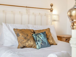 Una cama con ropa blanca, un cabecero de madera y almohadas estampadas.