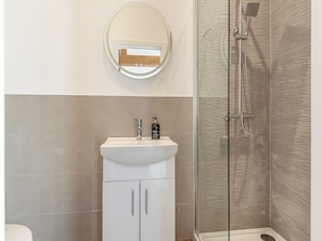 Un baño con lavamanos blanco, un espejo, ducha con pared texturizada y un inodoro.