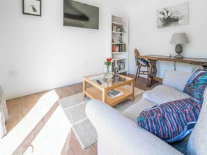 Un salon comprenant un canapé, une table basse, une bibliothèque et une lampe.