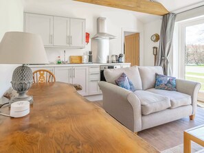 A modern kitchen with white cabinets, a wooden dining table, and a grey sofa with patterned cushions. - 1 bedroom accommodation in Baston, near Stamford (Baston, near Stamford)