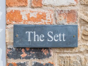 Un letrero oscuro de pizarra con la inscripción 'The Sett', fijado en una pared de ladrillo.