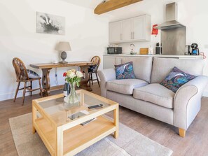 A living room with a sofa, a coffee table, a dining table with chairs, and a kitchen area. - 1 bedroom accommodation in Baston, near Stamford (Baston, near Stamford)