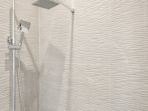 Ducha con pared texturizada, cabezal de ducha manual y cabezal de ducha instalado en la pared.
