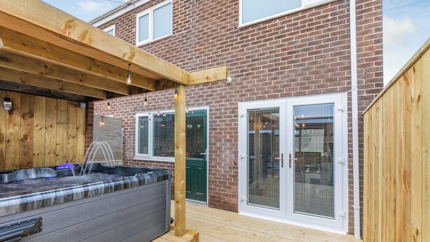 A wooden deck with a hot tub, a brick house, and a sliding glass door. - 2 bedroom accommodation in Warkworth (Warkworth)