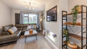 A modern living room with a leather sofa, a coffee table, and a TV mounted on the wall. - 2 bedroom accommodation in Warkworth (Warkworth)