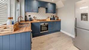 A modern kitchen with blue cabinets, a stainless steel refrigerator, and a built-in oven. - 2 bedroom accommodation in Warkworth (Warkworth)