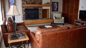 A living room with a stone fireplace, leather sofas, a coffee table, a lamp, a chair, and a TV stand. - 2 Bedroom + Sleeping loft condo near mountain village w/shuttle route (Gallatin Gateway)