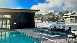 A pool area with a view of snow-covered mountains and a building with large windows. - 2 Bedroom + Sleeping loft condo near mountain village w/shuttle route (Gallatin Gateway)