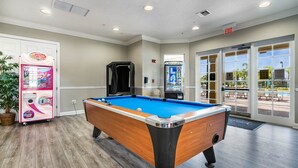 Una mesa de billar en una habitación con una puerta que da a un área exterior con piscina y sillas de descanso.