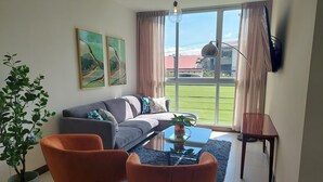 A modern living room with a grey sofa, orange chairs, a coffee table, and a large window with curtains. - Great 3 BD Apt in the BEST location in San José, Rohrmoser (San José)