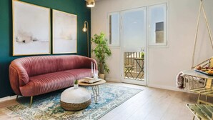 A modern living room with a red sofa, a round pouf, a coffee table, and a hanging light fixture. There are two framed abstract paintings on the wall and a potted plant. - Dorot 13 - Studio Apartment, Sleeps 2 (Jerusalem)