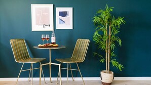 A dining area with two chairs, a small round table, a bottle of wine, and two framed pictures on the wall. - Dorot 13 - Studio Apartment, Sleeps 2 (Jerusalem)