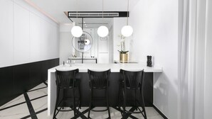 A modern kitchen with a white countertop, black bar stools, and pendant lighting. - King George Deluxe Suite (Jerusalem)