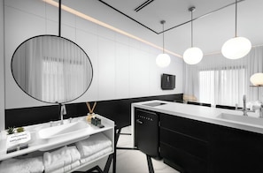 Een moderne badkamer met een grote spiegel, een wastafel en een toilet. Op het aanrecht liggen handdoeken en een fles handzeep.