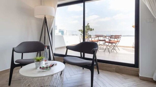 Een moderne kamer met een groot raam, twee zwarte stoelen, een klein rond tafeltje en een vloerlamp.