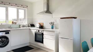 Een moderne keuken met witte kasten, een wasmachine, een inbouwoven, een koelkast en een raam met uitzicht op de omgeving.