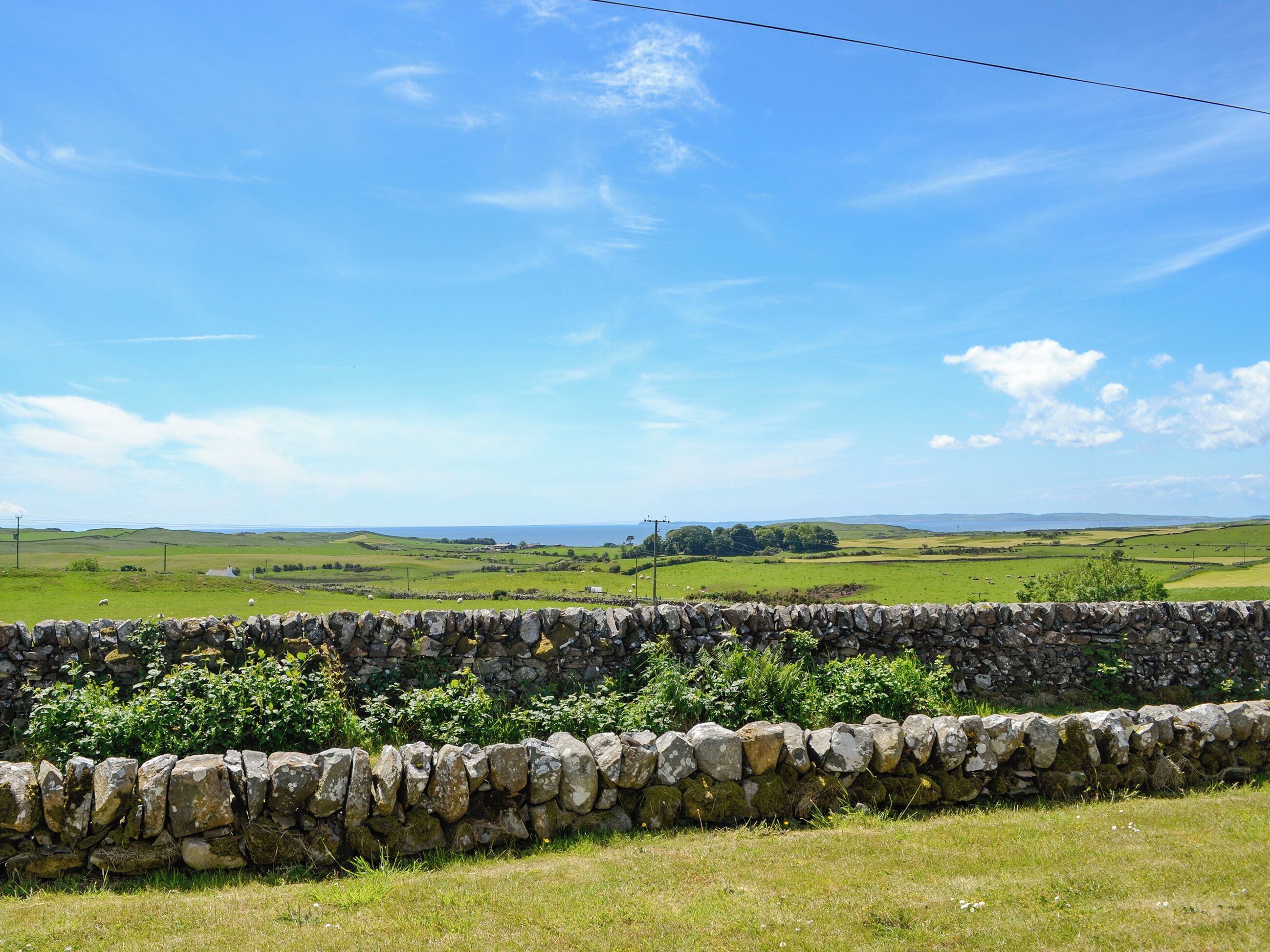 A stone wall, grassy field, and distant landscape with a clear sky.