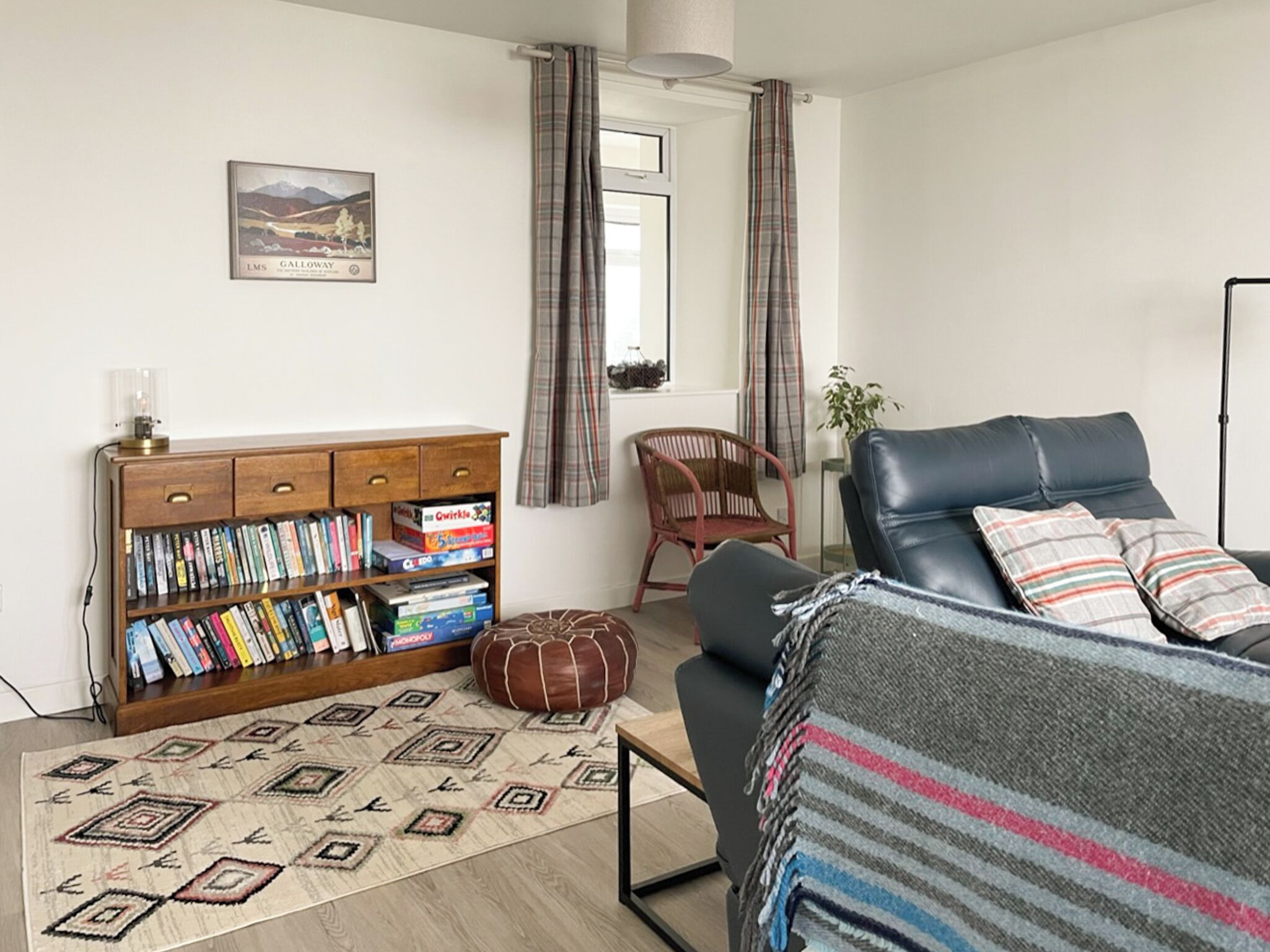 A living room with a sofa, a bookshelf, a patterned rug, and plaid curtains.
