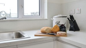 Een keuken met een spoelbak, een snijplank met brood en druiven, een pan en een messenblok.