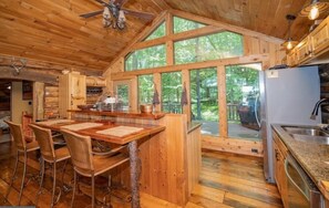 A wooden cabin interior with a dining area, kitchen, and large windows. - Authentic Cabin in the Woods! (Oakland)