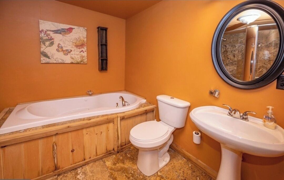 Un baño con bañera de madera, inodoro, lavamanos y espejo.