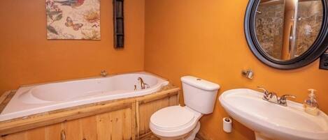 Un baño con bañera de madera, inodoro, lavamanos y espejo.