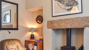 Un salon chaleureux avec une cheminée, un fauteuil confortable, une table avec une bouteille et un verre, et une télécommande.