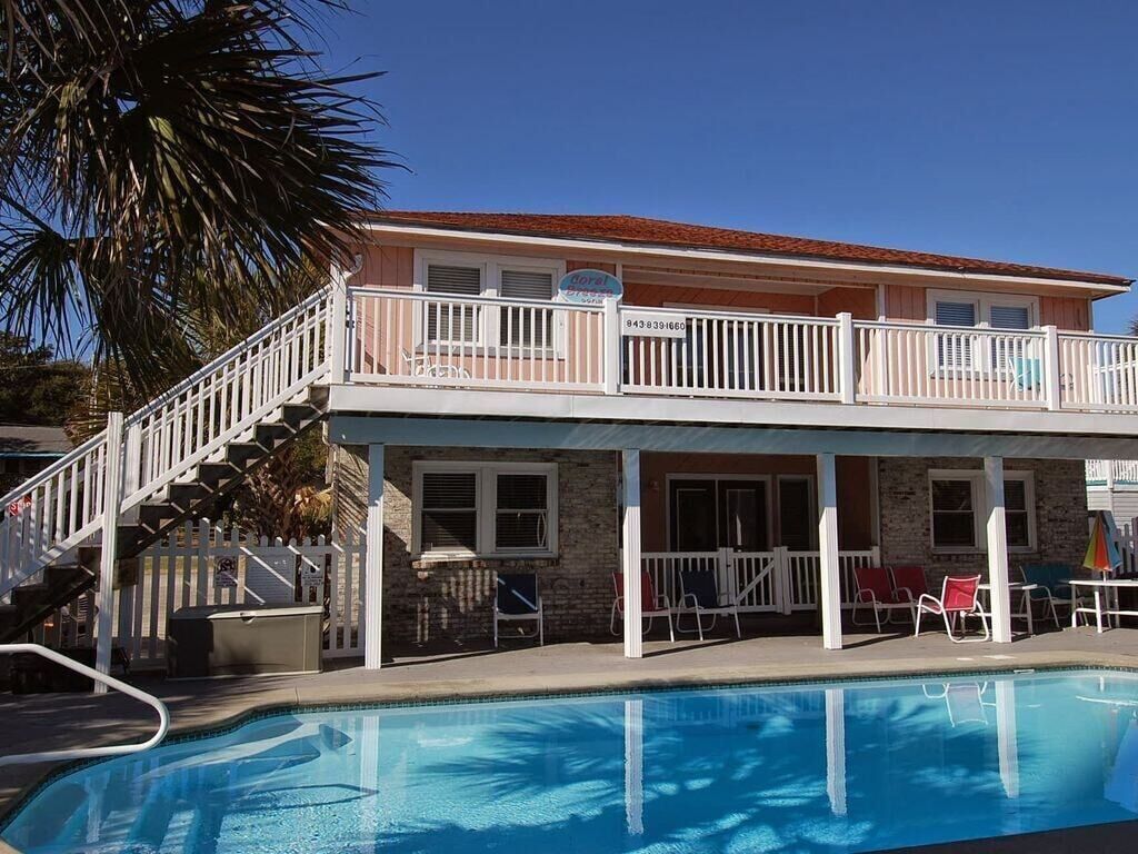 A hotel with a pool, a balcony with white railings, and a staircase leading to the upper level.