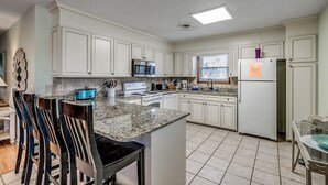 A kitchen with white cabinets, a granite countertop, a stainless steel refrigerator, and a microwave.