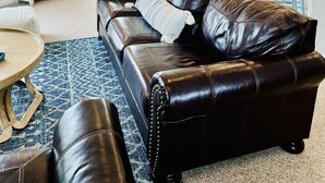 Een ruime woonkamer met een bruine leren bank, een eethoek met een houten tafel en stoelen, en een plafondventilator.