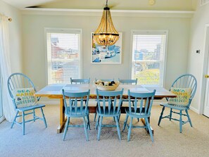 Une salle à manger avec une table en bois et des chaises bleues, un lustre et un tableau accroché au mur.