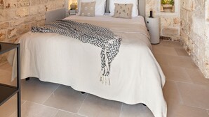 A bedroom with a stone wall, a bed with a patterned blanket, bedside lamps, and a hanging light fixture. - Beautifull Villa with Trullo (Ostuni)