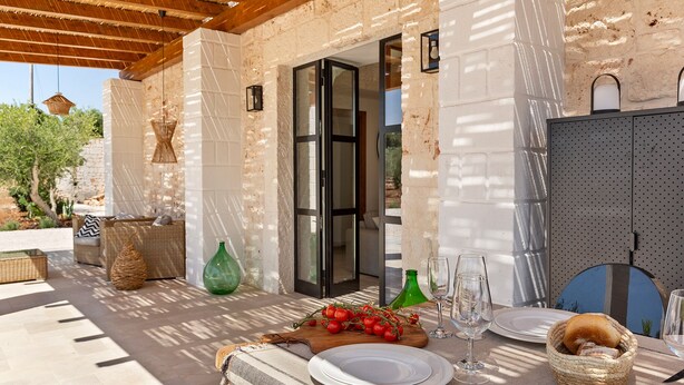 An outdoor dining area with a table set for two, featuring a plate, wine glasses, and a basket of bread. - Beautifull Villa with Trullo (Ostuni)
