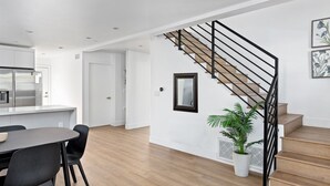 A modern kitchen with white cabinets, a dining area with a table and chairs, and a staircase with a black railing. - Brand new house next to Downtown Los Angeles (Los Angeles)