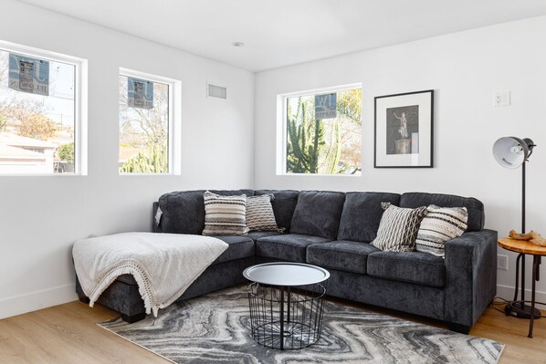 A modern living room with a dark grey sectional sofa, a round coffee table, and a patterned rug.