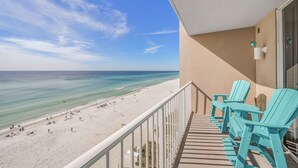 Varanda com cadeiras Adirondack cor turquesa com vista para uma praia com pessoas e guarda-sóis.