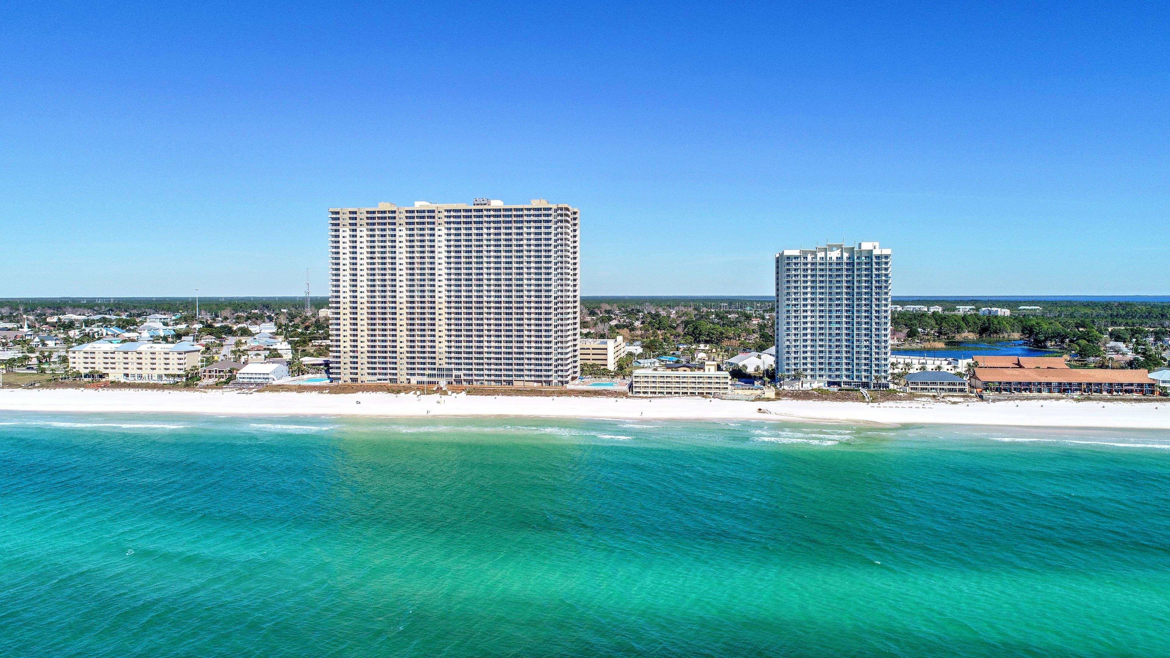 A coastal hotel with multiple high-rise buildings, a beach, and clear turquoise waters.