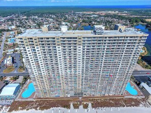 A high-rise hotel with multiple balconies, a swimming pool, and a view of the surrounding city and coastline. - Tidewater 713- FREE Beach Service for 4, Golf+Perks, 2BR/3BA+Bunks,Pools,Gym! (Panama City Beach)