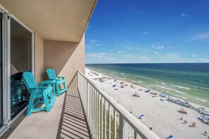 A balcony with turquoise chairs overlooking a beach with umbrellas and people.