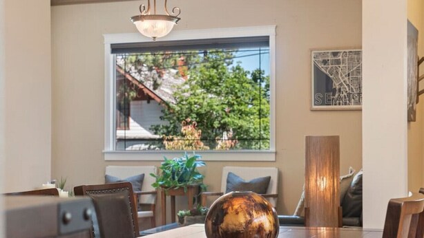 Un coin repas avec une table en bois, des chaises, un bol décoratif et une fenêtre donnant sur un paysage verdoyant et un bâtiment.