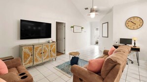 Een woonkamer met een flatscreen televisie, een bank, een kast en een klok aan de muur.