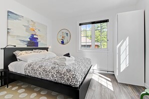 Una camera da letto moderna con un letto grande, una finestra con tende, un quadro appeso al muro e vista sull'esterno.