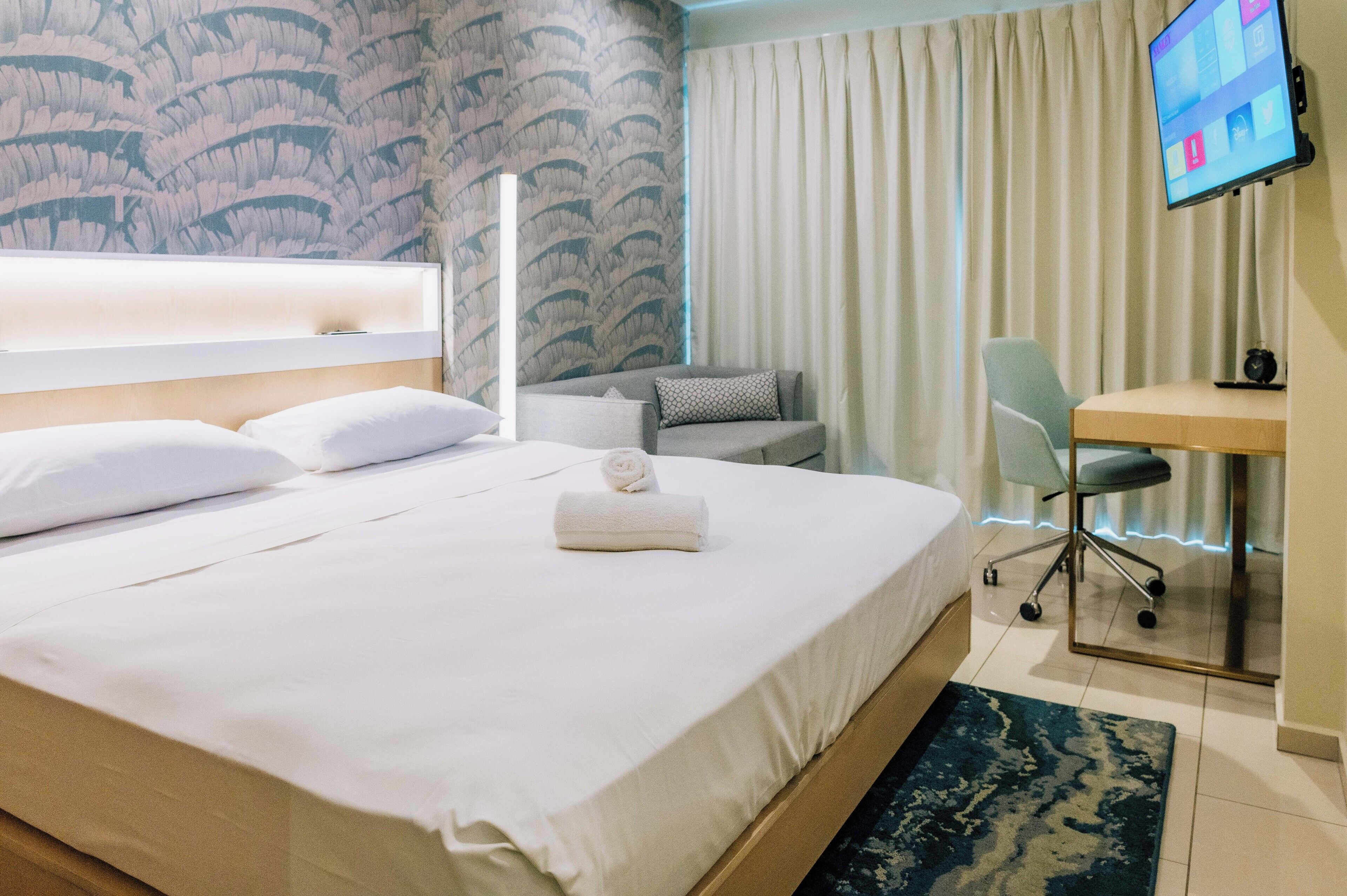 Une chambre d’hôtel avec un grand lit, un bureau, une chaise et un téléviseur fixé au mur.