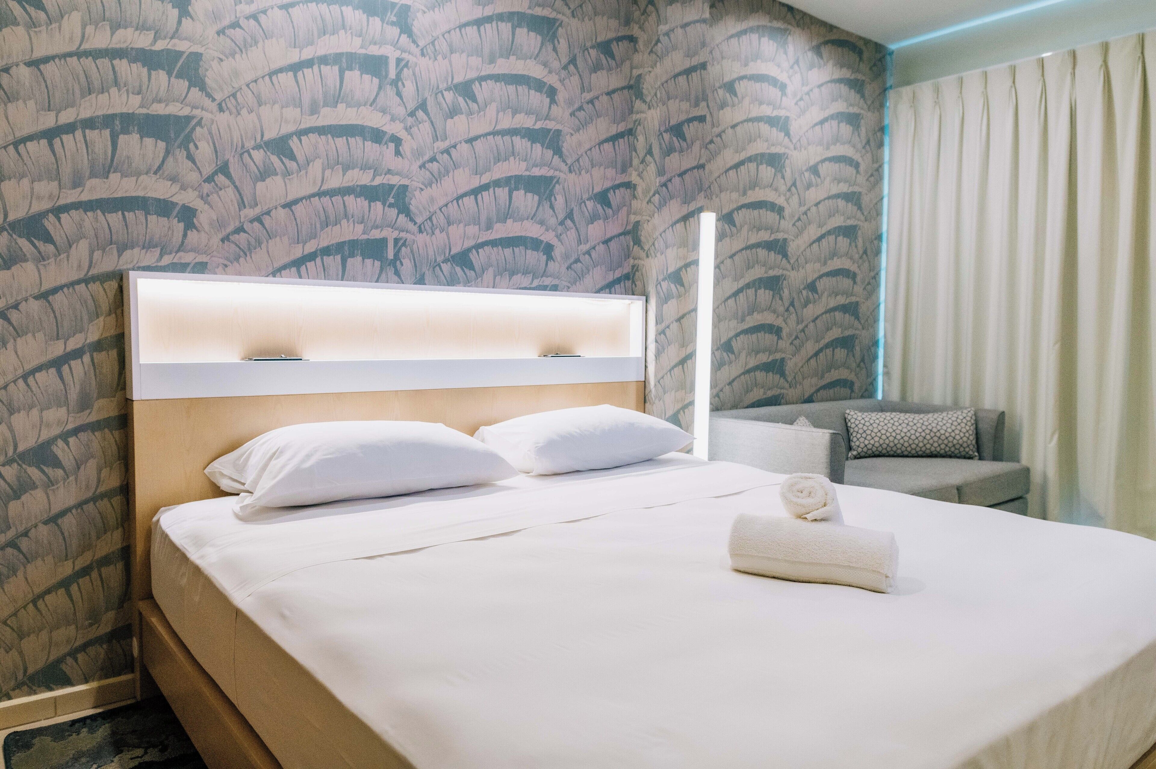 A hotel room with a bed, a headboard, a sofa, and a curtain.