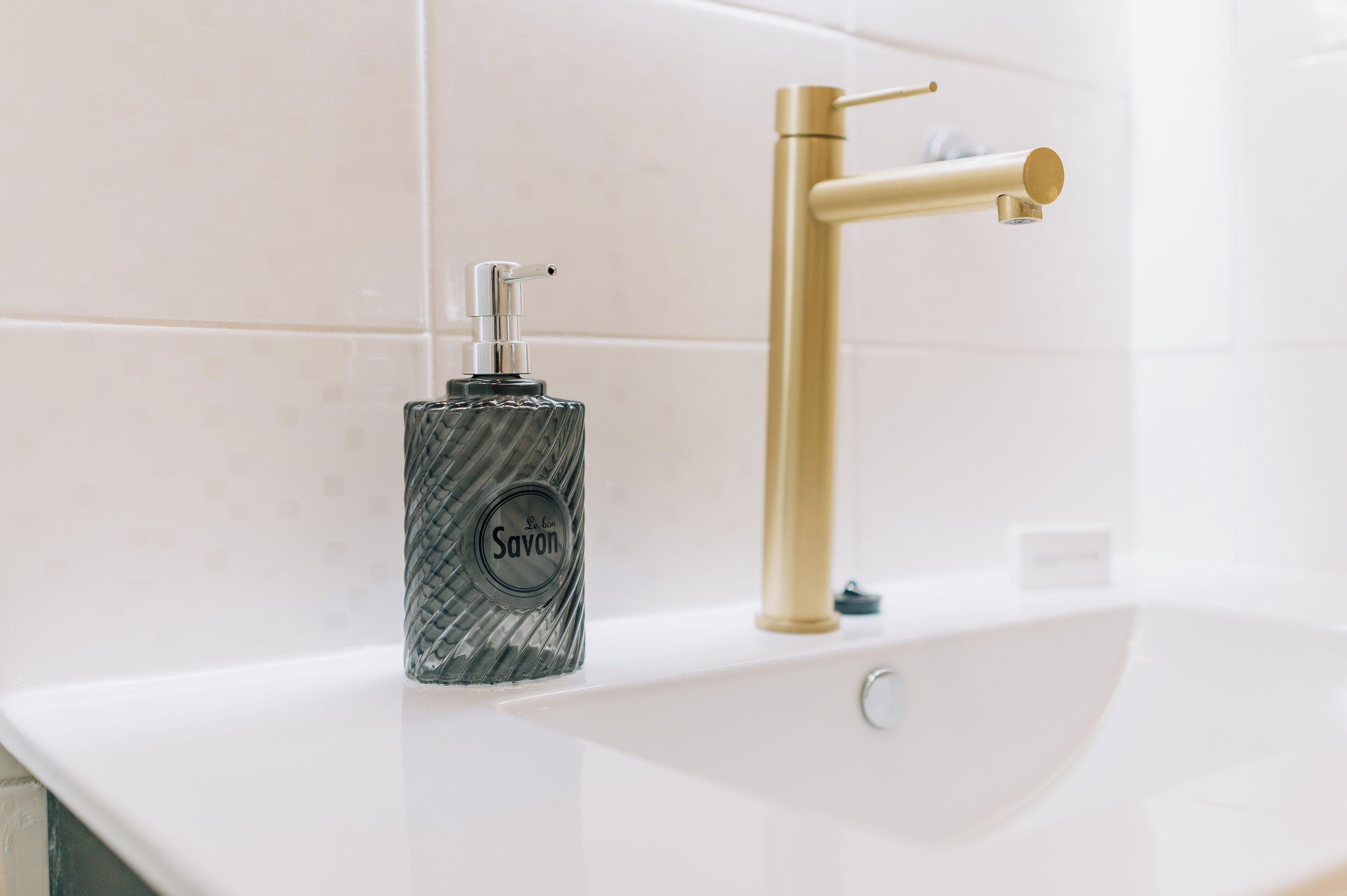 Un baño con un lavabo blanco, un grifo dorado y un dispensador de jabón Savon.
