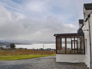 A building with a covered porch and a view of a lake and mountains in the distance.