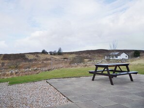 A picnic table on a paved area with a view of a hilly landscape and a white house in the background.