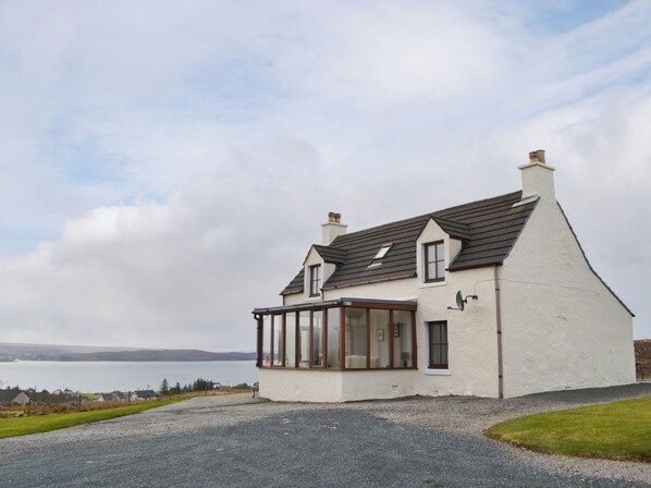 A single-story house with a sloped roof, a conservatory with glass walls, and a view of a body of water in the background.